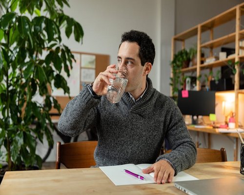 A person taking a physical break, drinking water next to an organized office window view